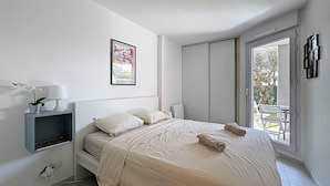Une chambre à coucher avec un lit, une table de chevet avec une lampe, un tableau encadré et une fenêtre donnant sur l’extérieur.