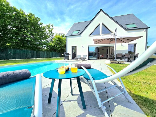 A modern house with a swimming pool, a patio with a table and chairs, and a covered outdoor area.