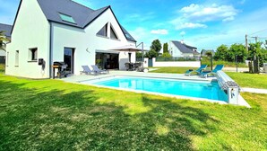 Una casa moderna de dos pisos con piscina, un patio cubierto y un césped bien cuidado.
