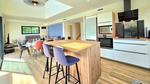 Una cocina moderna con una isla central, taburetes de bar y una zona de comedor con mesa y sillas.