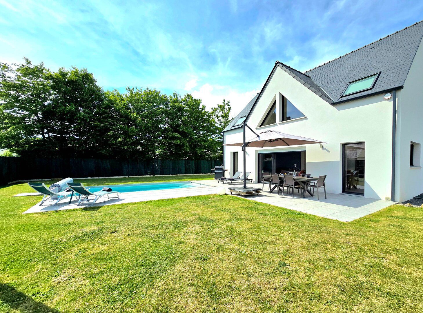 A modern house with a swimming pool, outdoor seating, and a large window overlooking the yard.