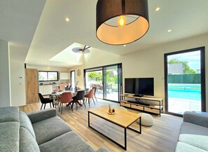A modern living room with a dining area, a TV, and a pool view.