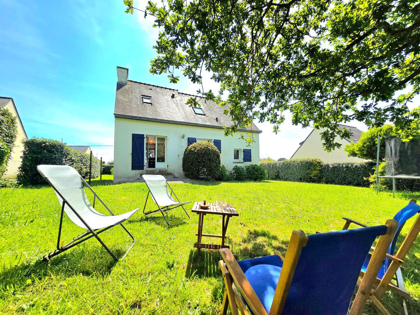 Une maison avec une pelouse, deux chaises de jardin et une petite table.