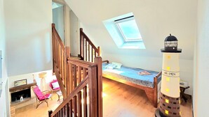 Ein Schlafzimmer im Loft-Stil mit Oberlicht, einer Holztreppe, einem Bett, einem kleinen Tisch und einem Leuchtturmmodell.