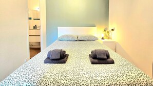 A bedroom with a bed, pillows, a bedside table with a lamp, and a bathroom visible through an open door. - A pas de tout, historic center, train, parking (Vannes)