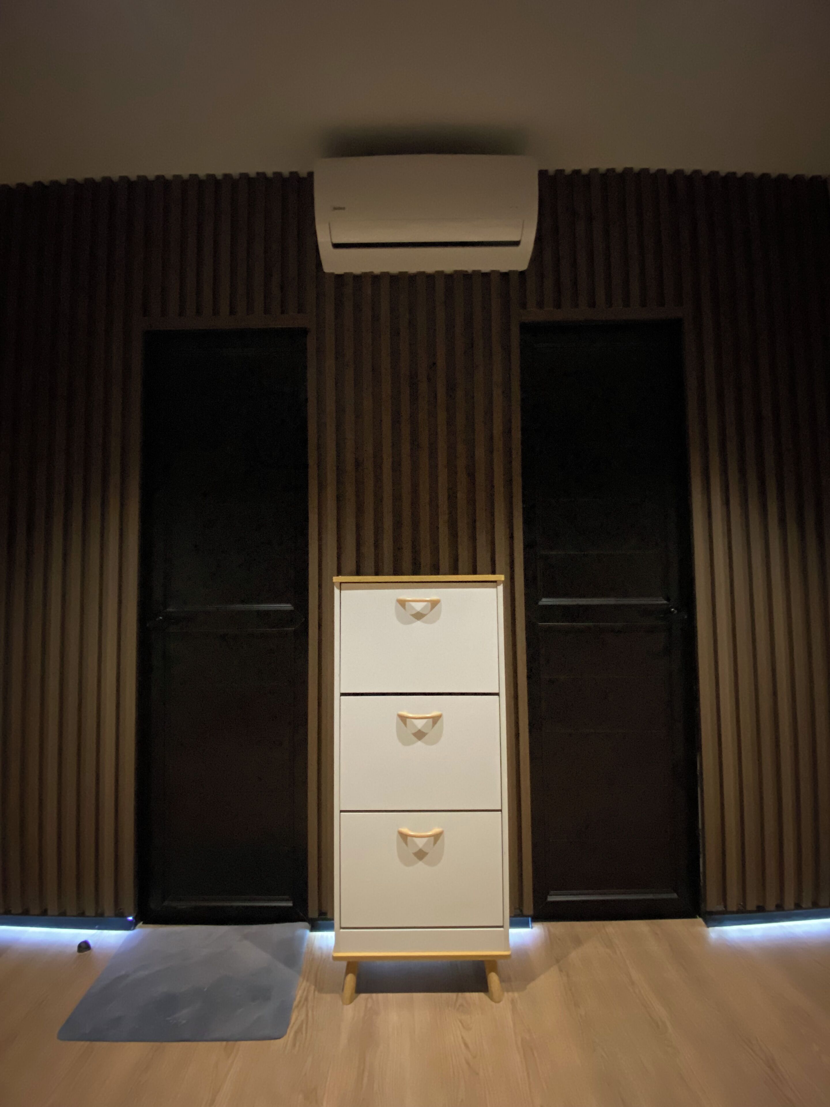 Una habitación con piso de madera, un armario blanco con cajones y un equipo de aire acondicionado instalado en el techo.