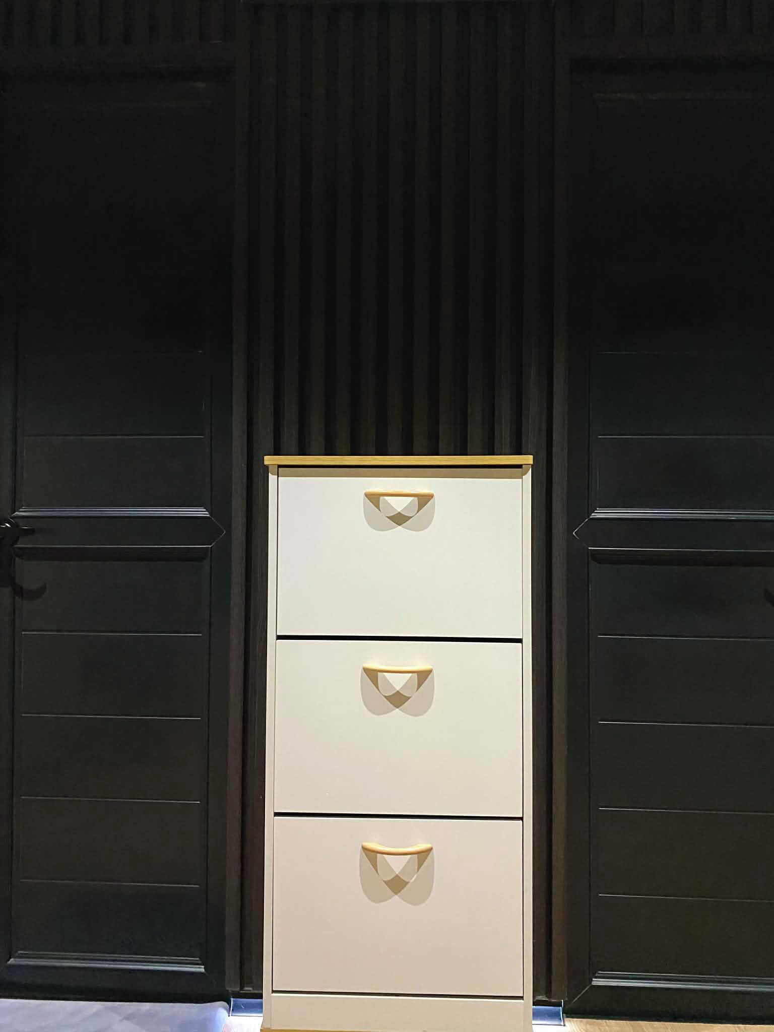A tall, white filing cabinet with three drawers, placed between two dark wooden doors.