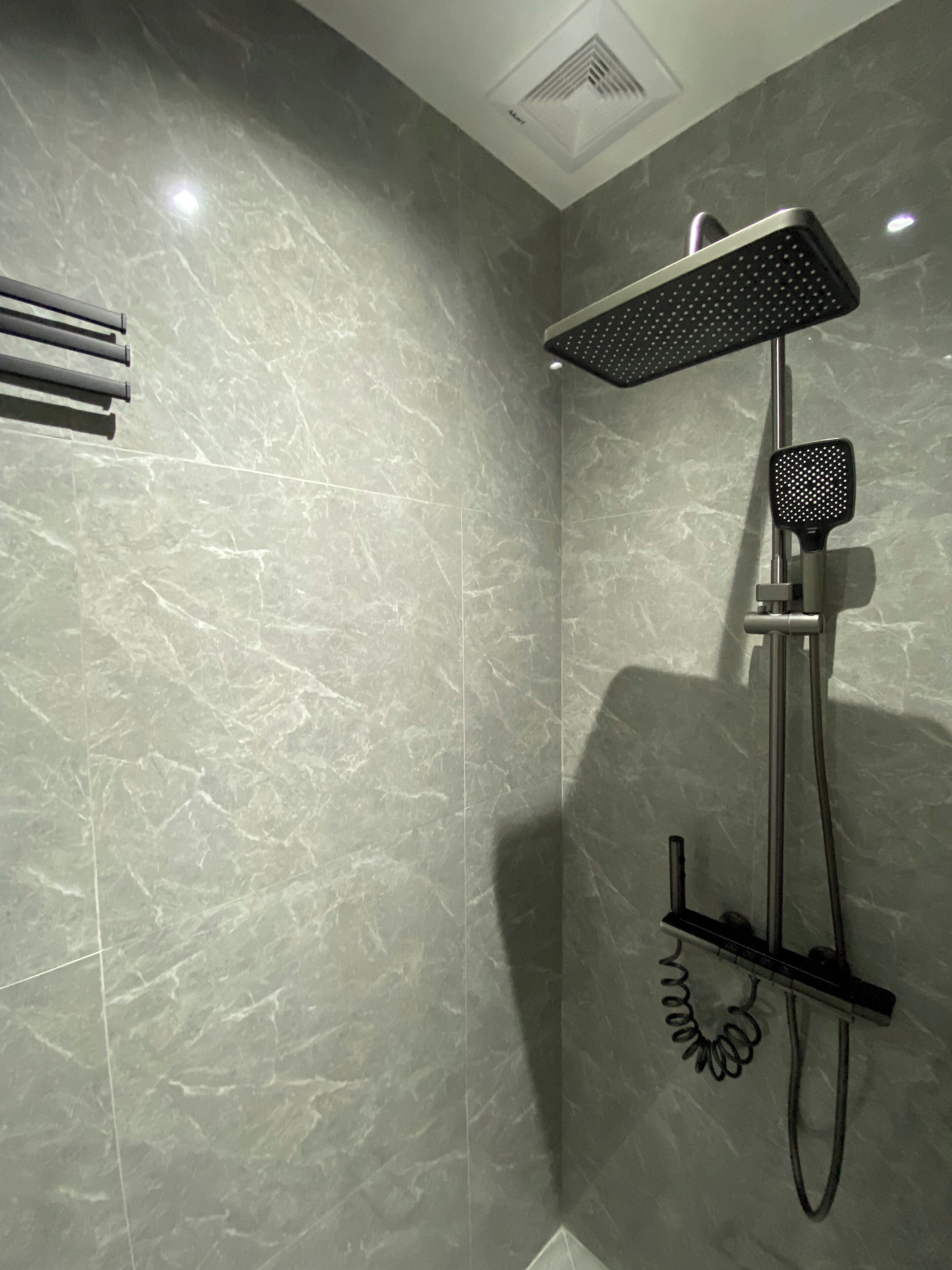 Une douche moderne dotée d’un pommeau de douche à main et d’un pommeau de douche fixe, tous deux fixés sur un mur revêtu de marbre.