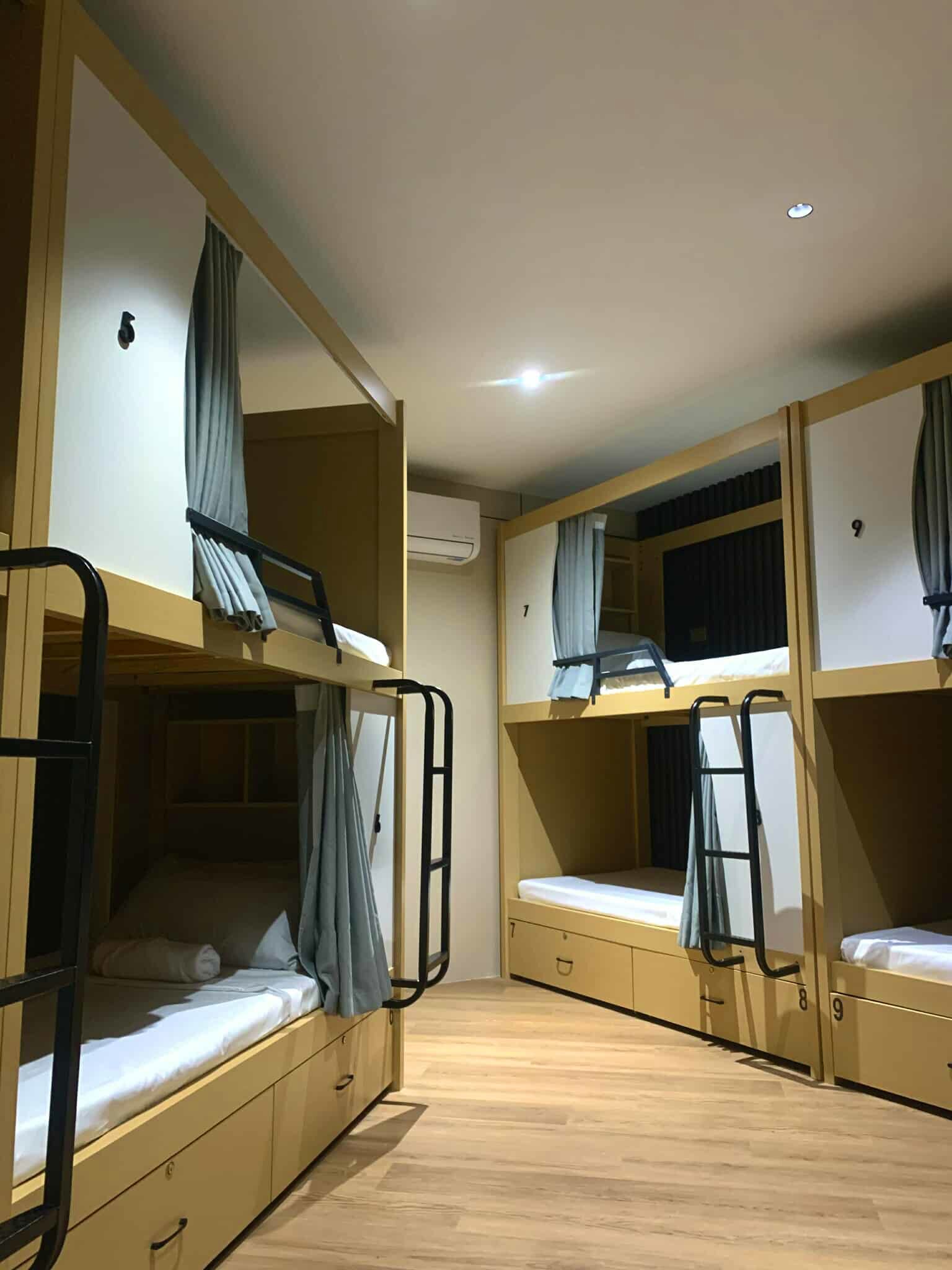 A dormitory room with bunk beds, wooden flooring, and curtains.