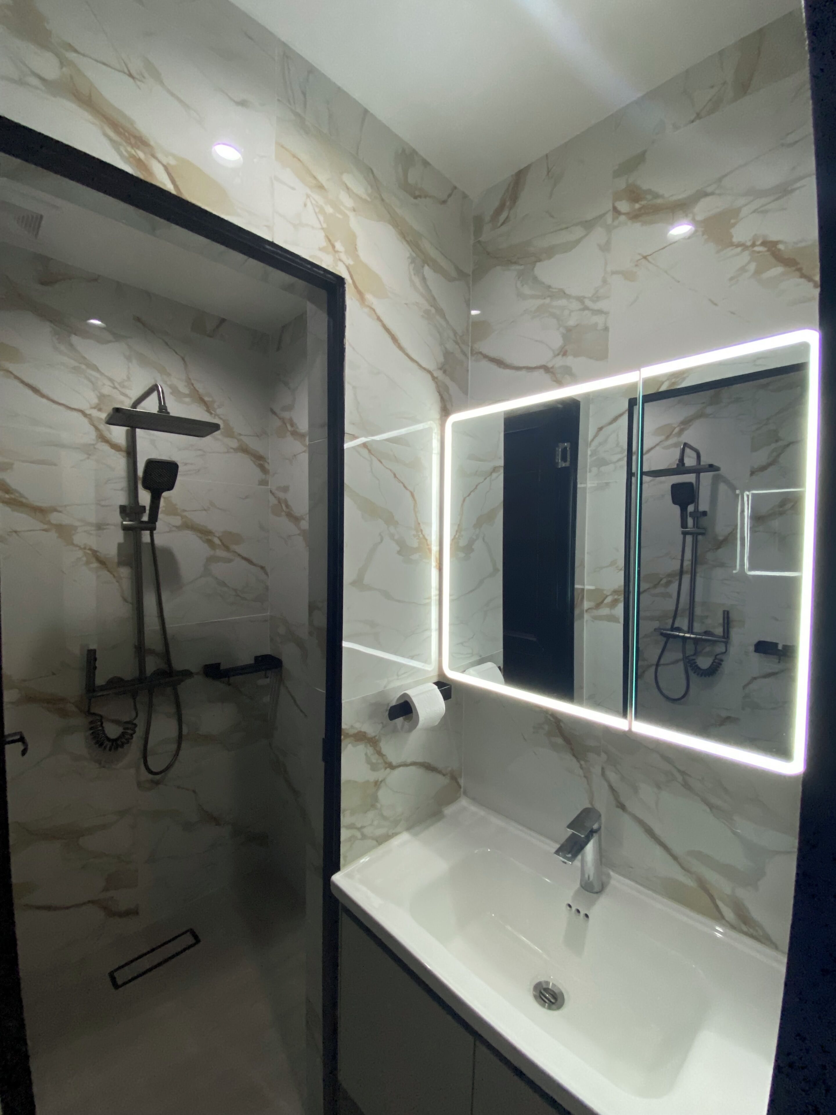 Un baño con pared de mármol, un lavamanos moderno y una zona de ducha.