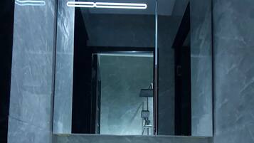 A modern bathroom with a large mirror, a white sink, and dark marble walls.