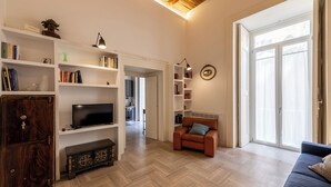A spacious living room with a wooden herringbone floor, a brown leather sofa, a blue couch, and a television on a white shelf. - Palazzo Guida al Duomo (Naples)