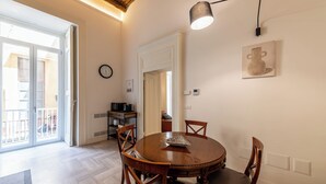 A dining area with a round wooden table, four chairs, a modern pendant light, and a wall-mounted clock. - Palazzo Guida al Duomo (Naples)