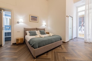 Un dormitorio con cama, dos lámparas de noche, un cuadro y vistas a través de una puerta.