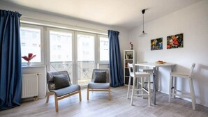 Un salon moderne avec un coin repas, de grandes fenêtres avec des rideaux et des œuvres d’art accrochées au mur.