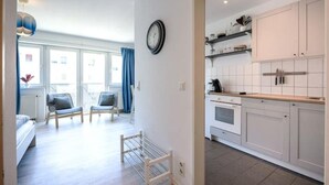 Une cuisine moderne avec des meubles blancs et un plan de travail en bois. Il y a une horloge au mur et une fenêtre avec des rideaux bleus.
