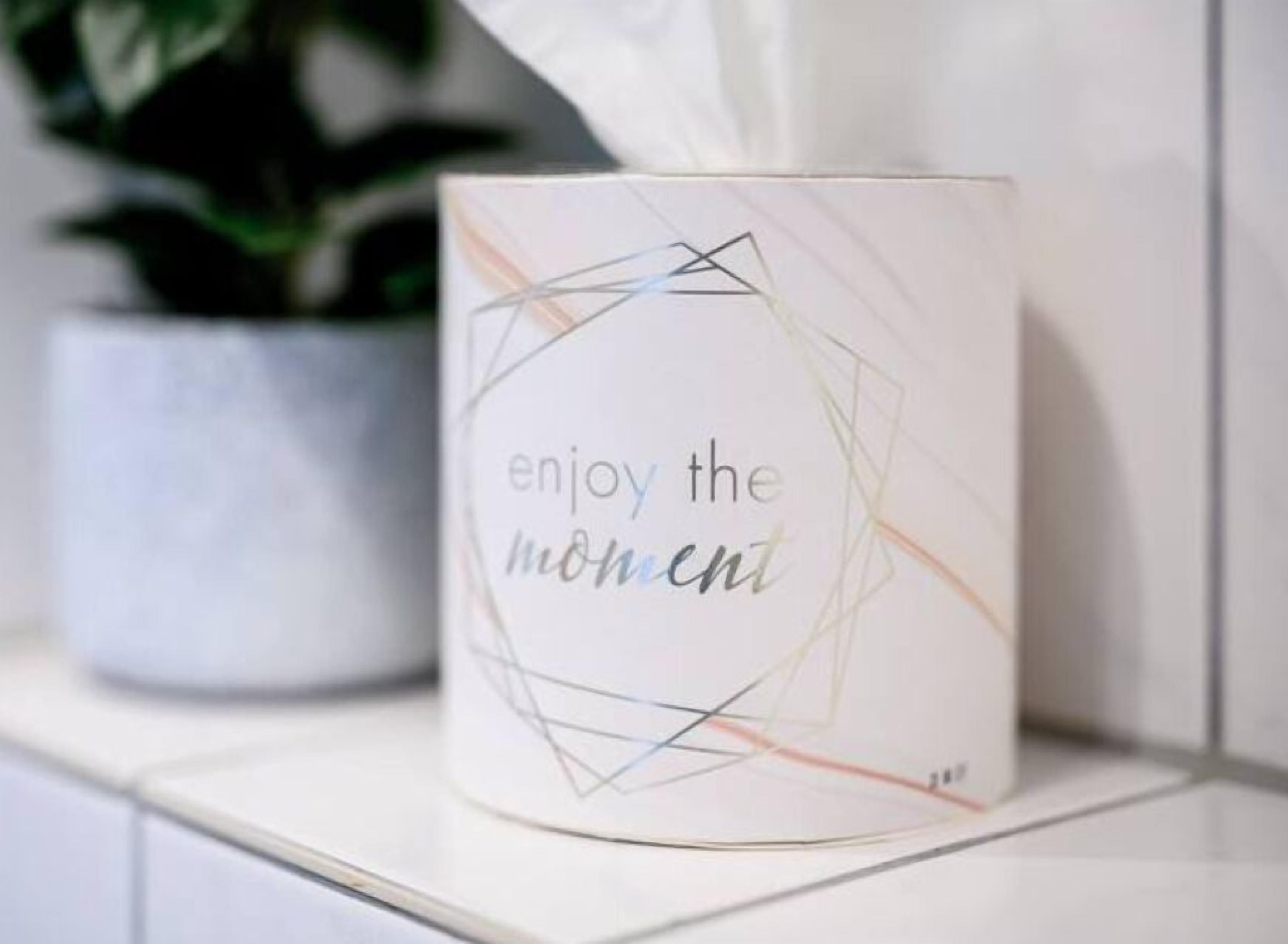 A white mug with the text "enjoy the moment" on a tiled surface.