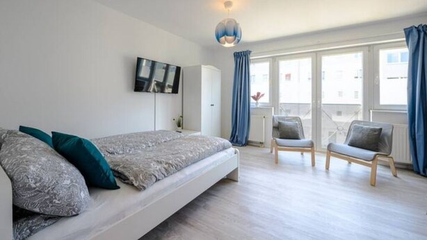 Une chambre moderne avec un lit, une télévision et un balcon équipé de chaises.