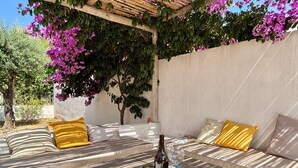Un espace extérieur aménagé avec une table, des coussins et une bouteille de vin.