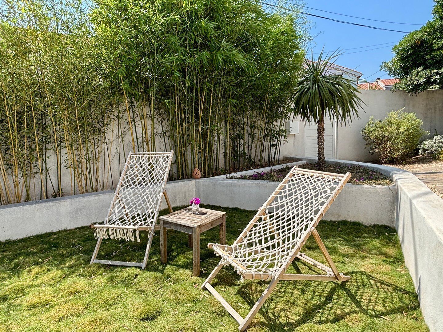 Twee rieten loungestoelen in een gazon met een betonnen muur en bamboeplanten.