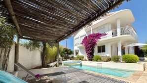 Une villa moderne dotée d’une piscine, d’un patio couvert et d’un balcon agrémenté de fleurs roses.