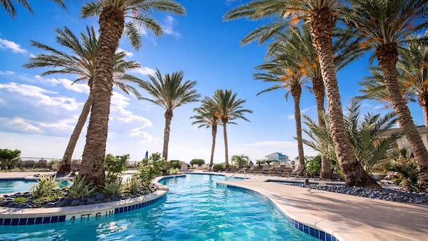 Une piscine bordée de palmiers, avec une eau d’un bleu cristallin et un ciel ensoleillé.