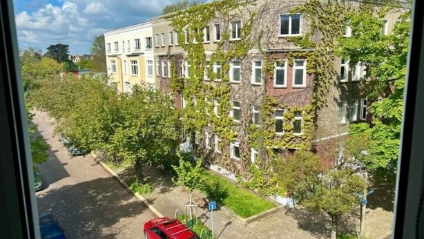 A multi-story building with ivy-covered walls and a parking area in front.