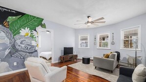 A modern living room with a ceiling fan, a flat-screen TV, and a mural on the wall.