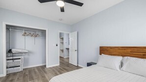 A bedroom with a bed, a wooden headboard, a closet with hanging clothes, and a ceiling fan.