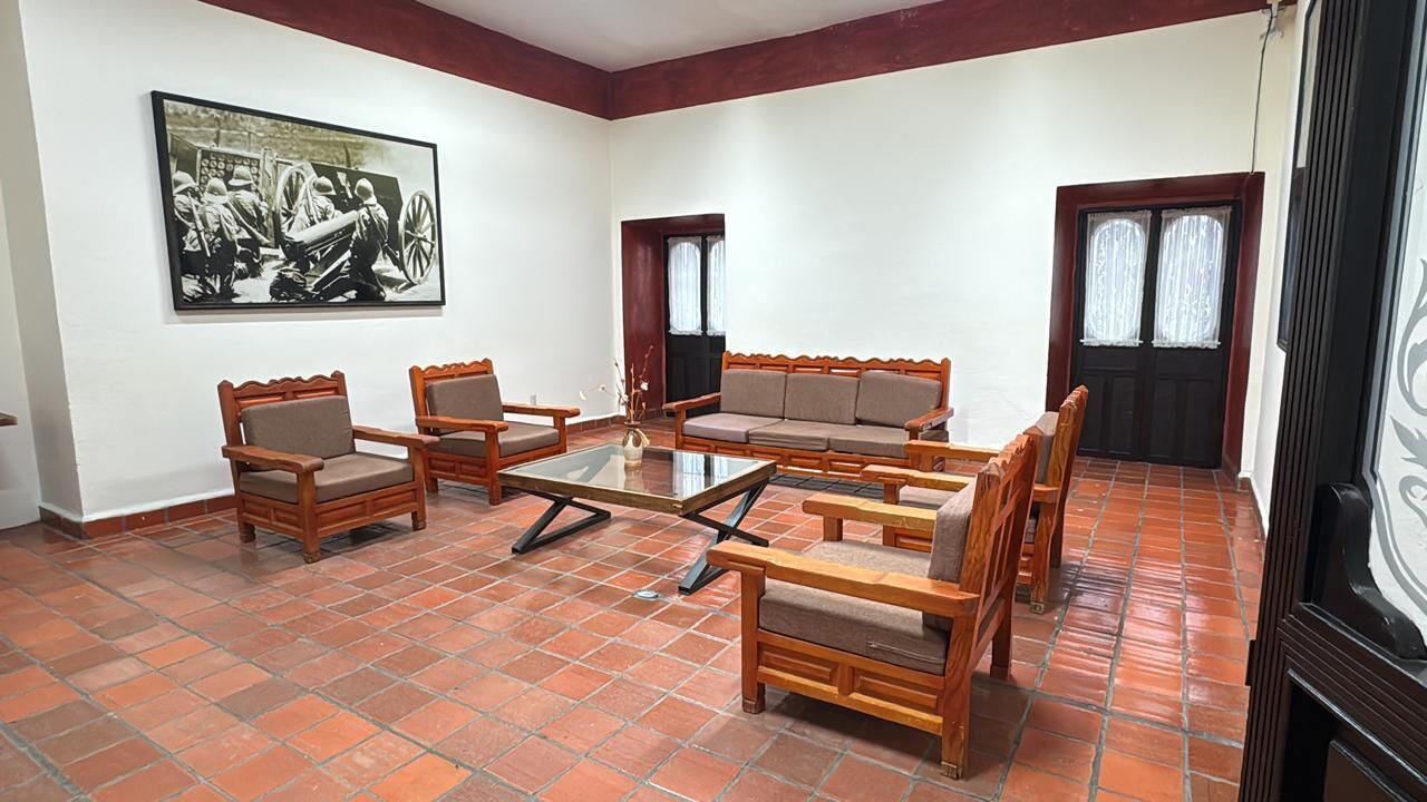 Una habitación con suelo de baldosas, muebles de madera, una mesa de centro de cristal y un cuadro en la pared.
