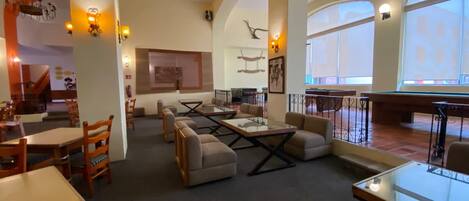 A spacious lobby with high ceilings, a billiards table, comfortable seating, and large windows.