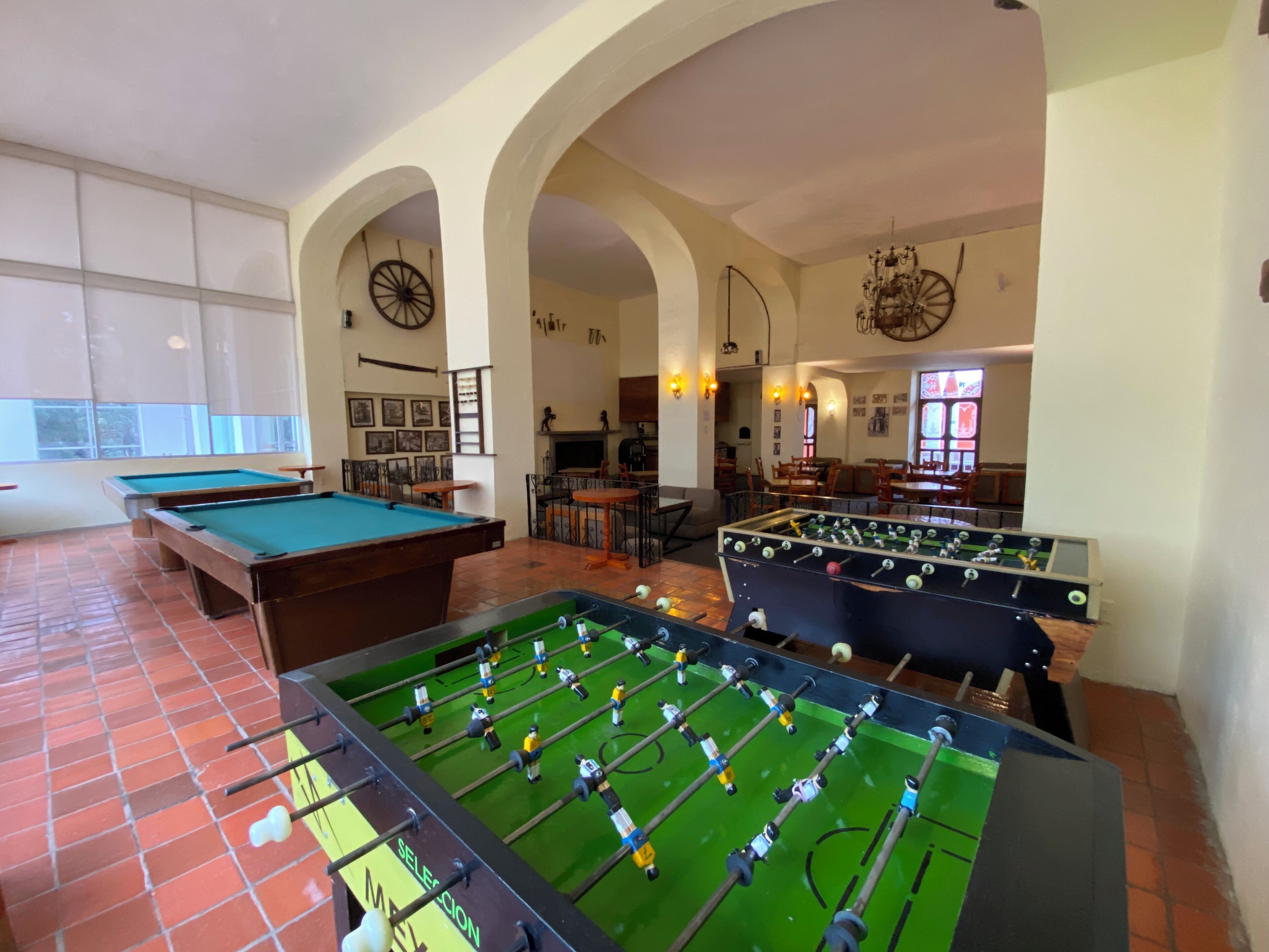 A pool table, foosball table, and billiards table in a room with arched ceilings and large windows.