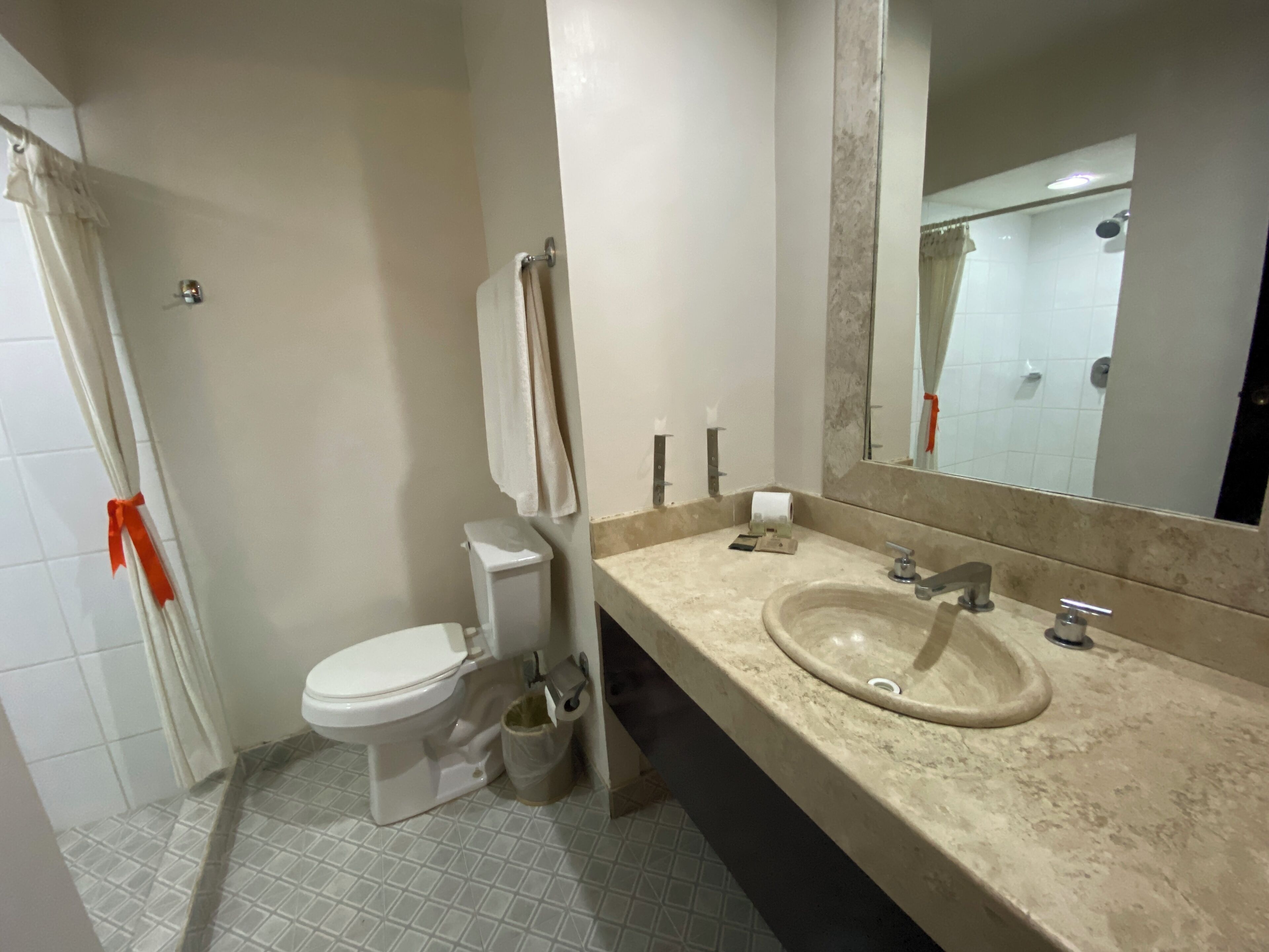 A bathroom with a toilet, sink, mirror, and tiled floor.