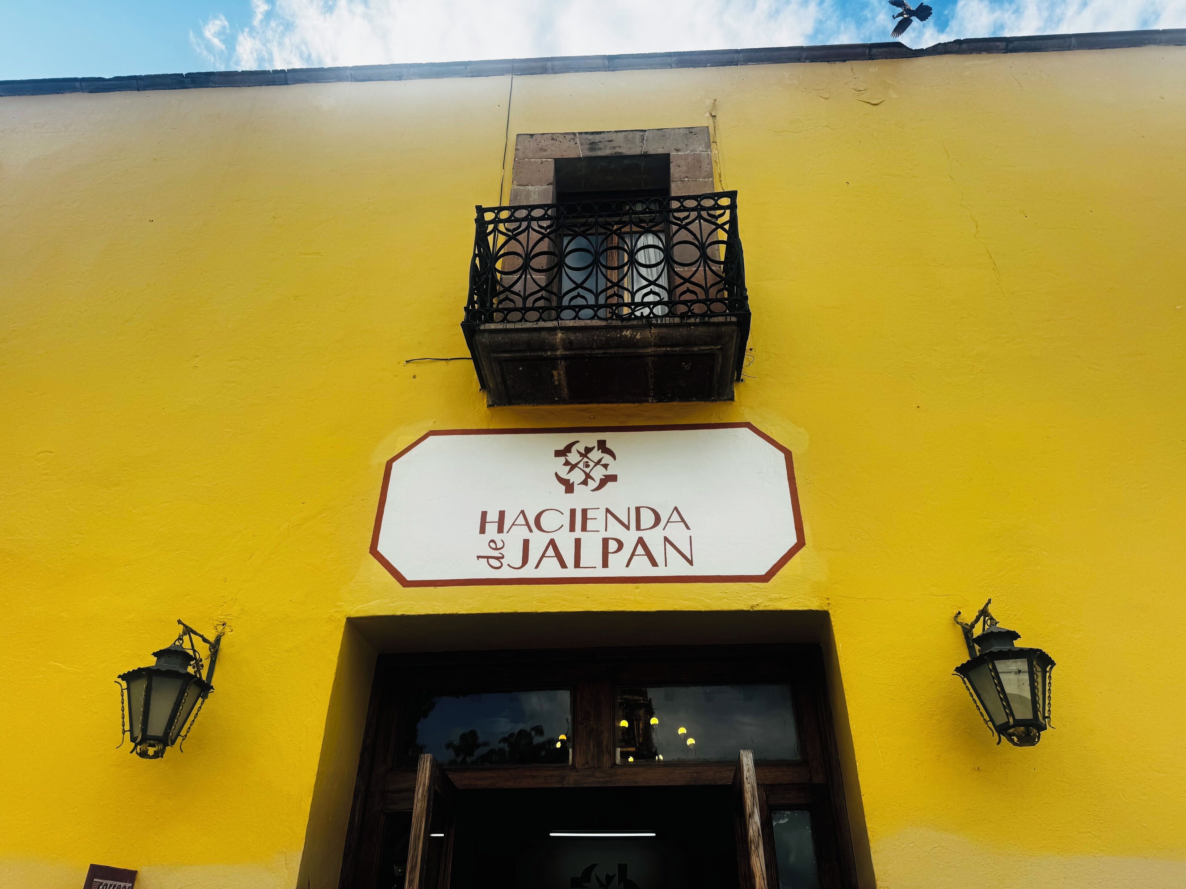 En gul byggnad med en skylt som visar texten ”Hacienda & Jaipur” och två lyktor som är monterade på väggen.