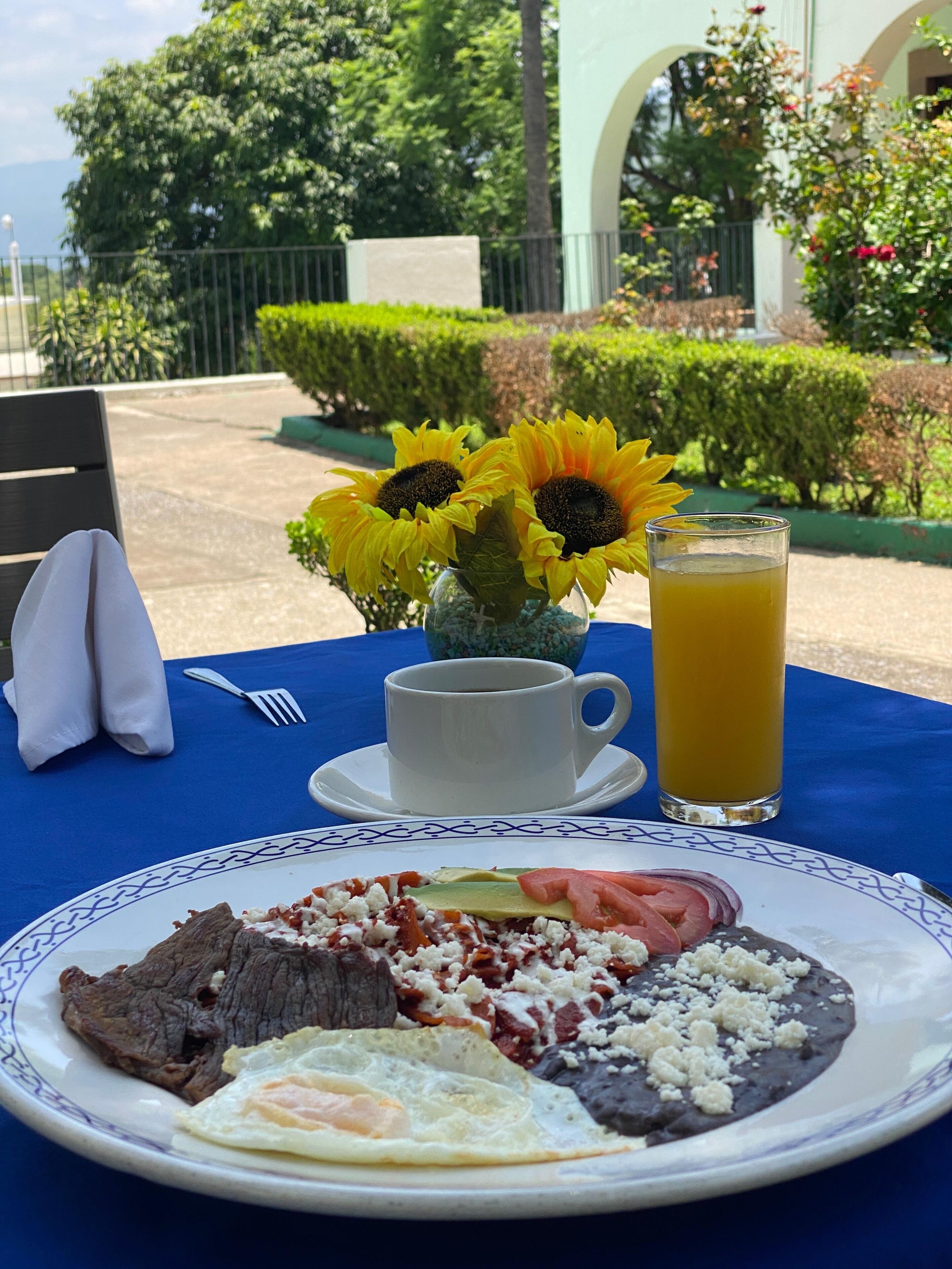 A table set with a plate of food, a cup of coffee, a glass of orange juice, and a vase with sunflowers.