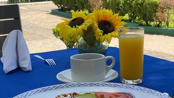 A table set with a plate of food, a cup of coffee, a glass of orange juice, and a vase with sunflowers.