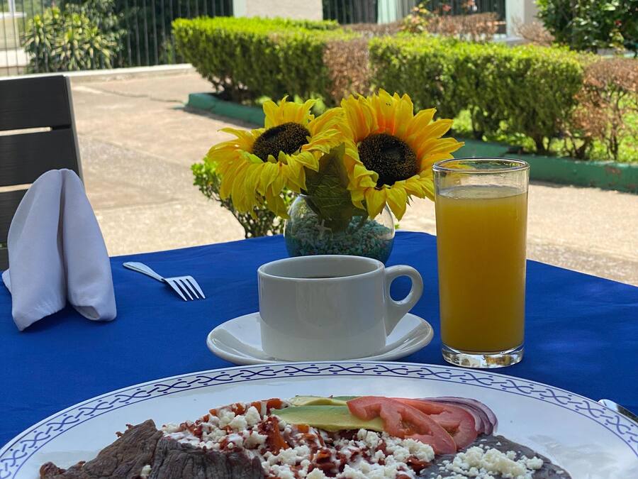 A table set with a plate of food, a cup of coffee, a glass of orange juice, and a vase with sunflowers.