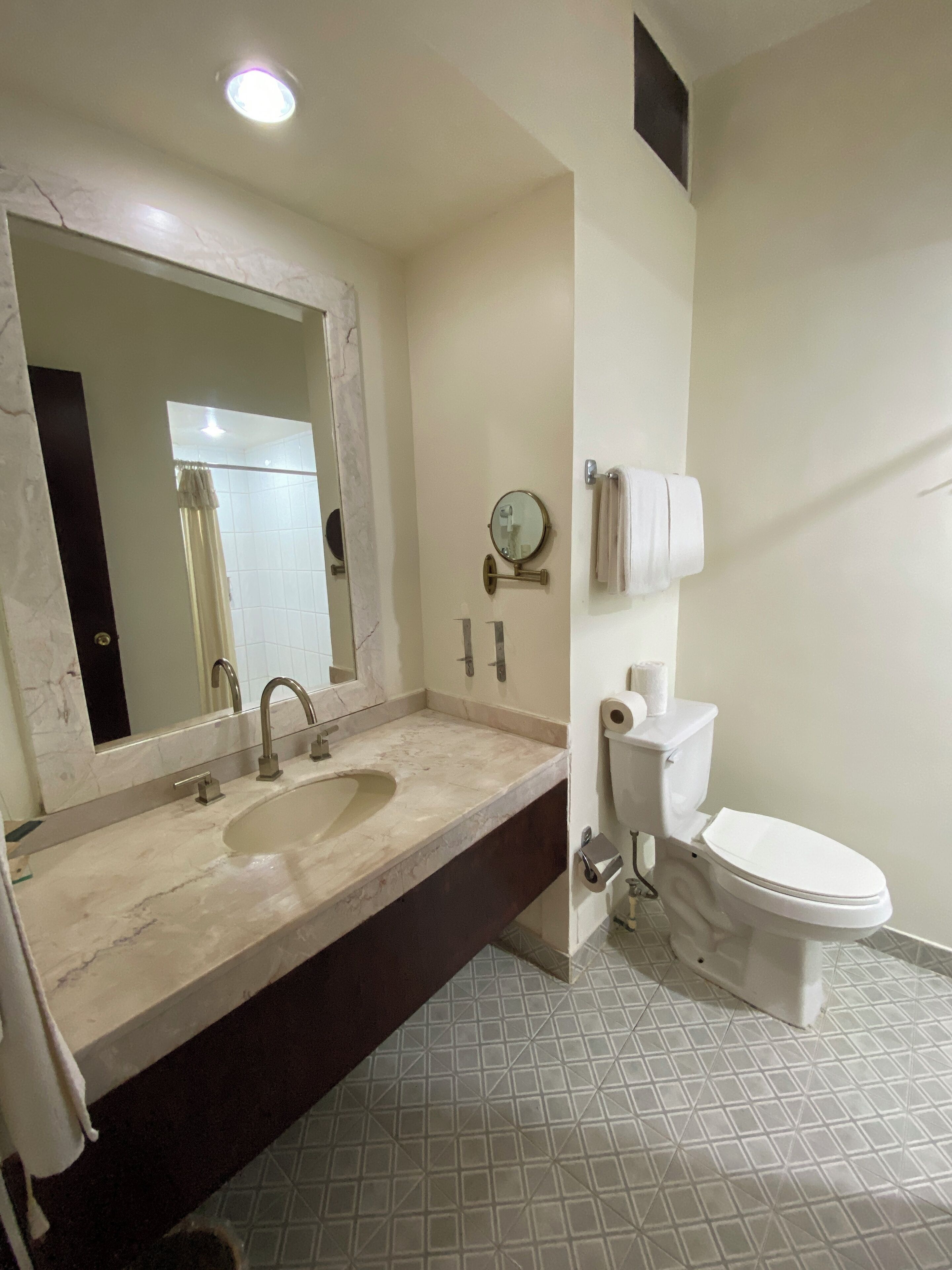 A bathroom with a marble sink, a mirror, a toilet, and a towel rack.