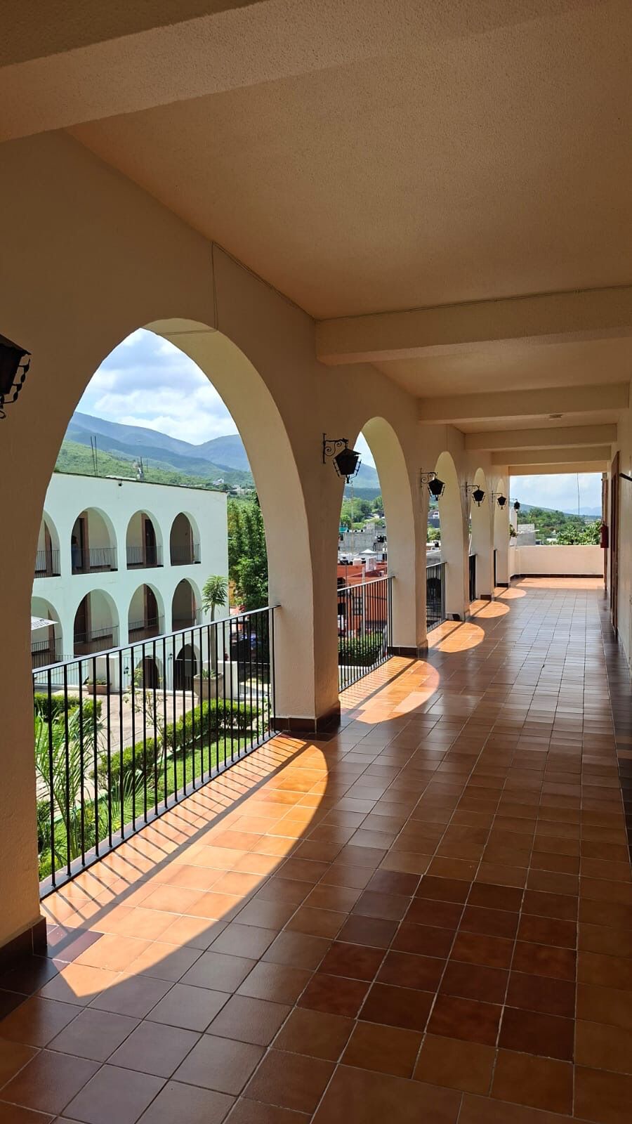 A covered corridor with arches, a tiled floor, and a view of a building with multiple arches and greenery.