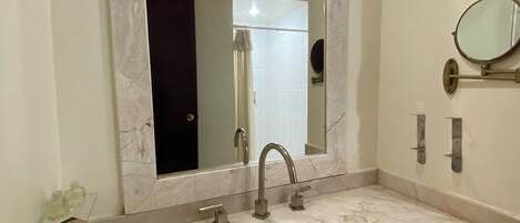 A bathroom with a marble sink, a large mirror, and a handheld mirror.
