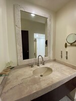 Un baño con lavamanos de mármol, un espejo grande y un espejo de mano.