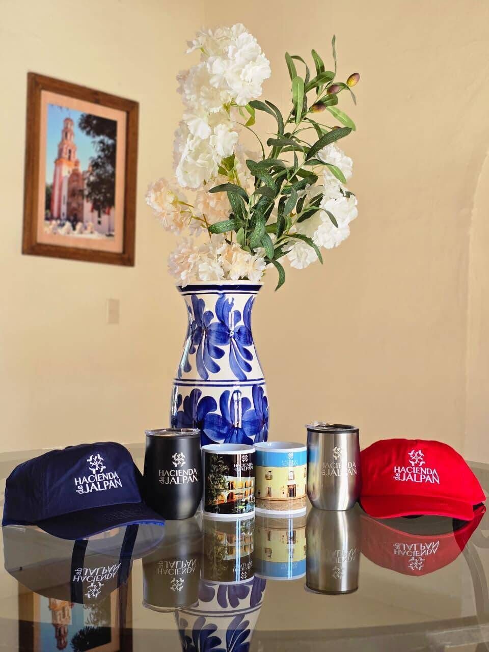 A table with a vase of white flowers, a blue and white patterned vase, and several branded items including a cap, a bottle, and a tin.