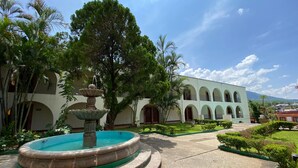 A courtyard with a fountain, surrounded by trees and a building with arched windows. - Hotel Hacienda de Jalpan (Jalpan de Serra)