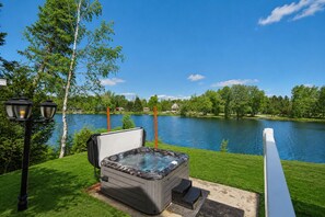 Un jacuzzi con vista a un lago, rodeado de césped y árboles.