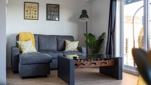 A modern living room with a grey sectional sofa, a foosball table, and a large window. - Le Citronnier, vue sur l'eau (Magog)