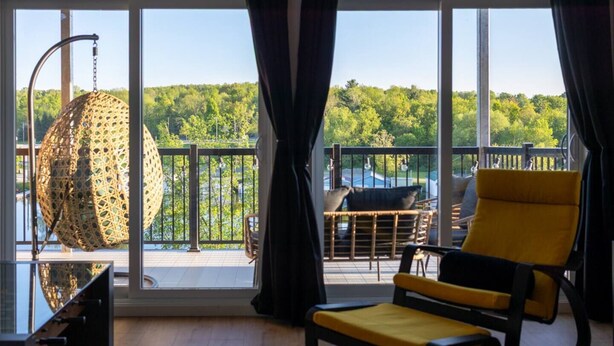 A room with a large window, a yellow chair, and a hanging chair. - Le Citronnier, vue sur l'eau (Magog)