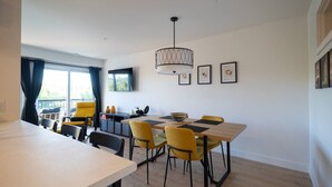 A modern dining area with a wooden table, yellow chairs, and a pendant light. - Le Citronnier, vue sur l'eau (Magog)