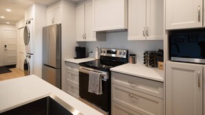 A modern kitchen with white cabinetry, stainless steel appliances, and a black countertop. - Le Citronnier, vue sur l'eau (Magog)