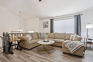 A living room with a sofa, a coffee table, a side table, a lamp, and a window with curtains.