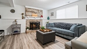 A living room with a fireplace, a grey sofa, a wooden coffee table, and a small side table. - Near Carowinds ~ 4BR w/ Game Room & Splash Pad (Pineville)